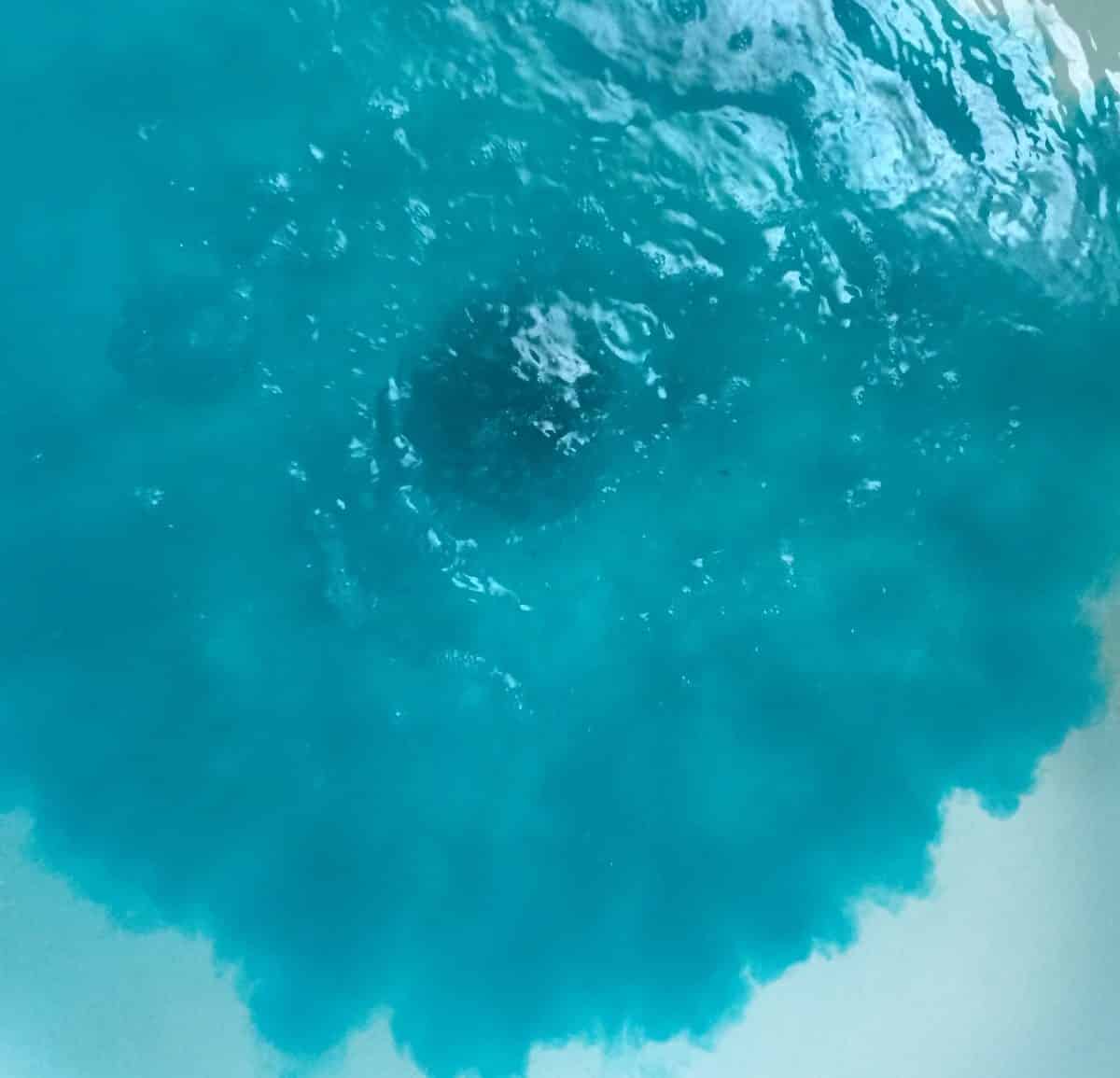 homemade bath bomb dropping into bath water and turning water sea blue