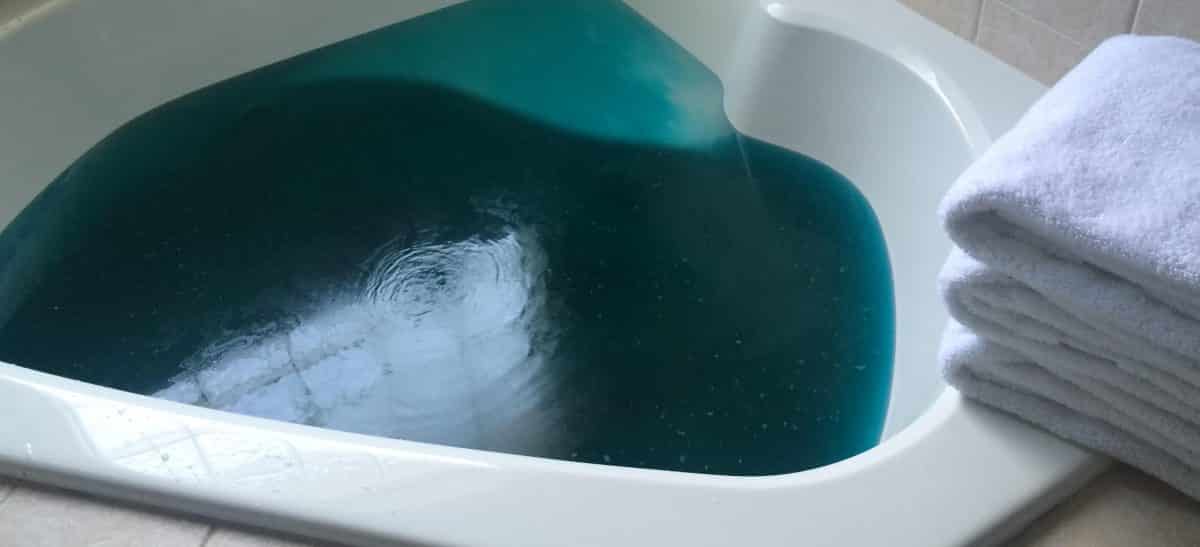 soaker tub filled with blue bath water and pile of white fluffy towels