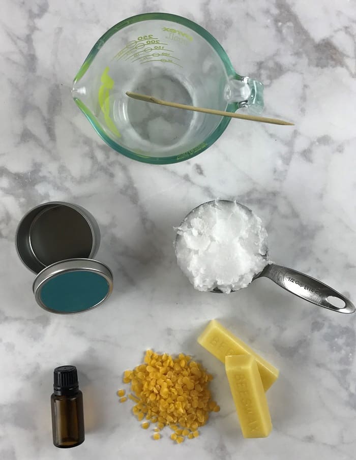 ingredients and supplies for essential oil sleep salve- coconut oil, beeswax, essential oil, container, and glass measuring cup