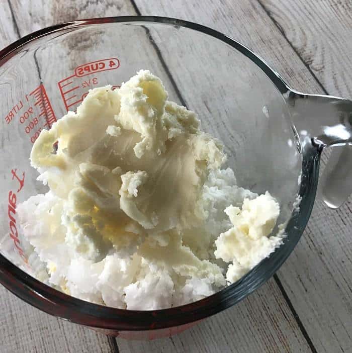 mango butter being added to measuring cup with other butters