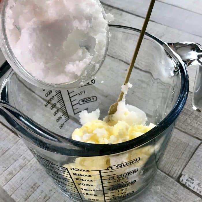 Adding coconut oil to avocado butter in clear heat-safe measuring cup for Copycat Lush Ocean Salt scrub recipe made with essential oils