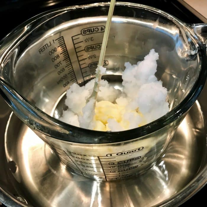 Melting avocado butter and coconut oil in clear heat-safe measuring cup using double boiler method for Copycat Lush Ocean Salt scrub recipe made with essential oils