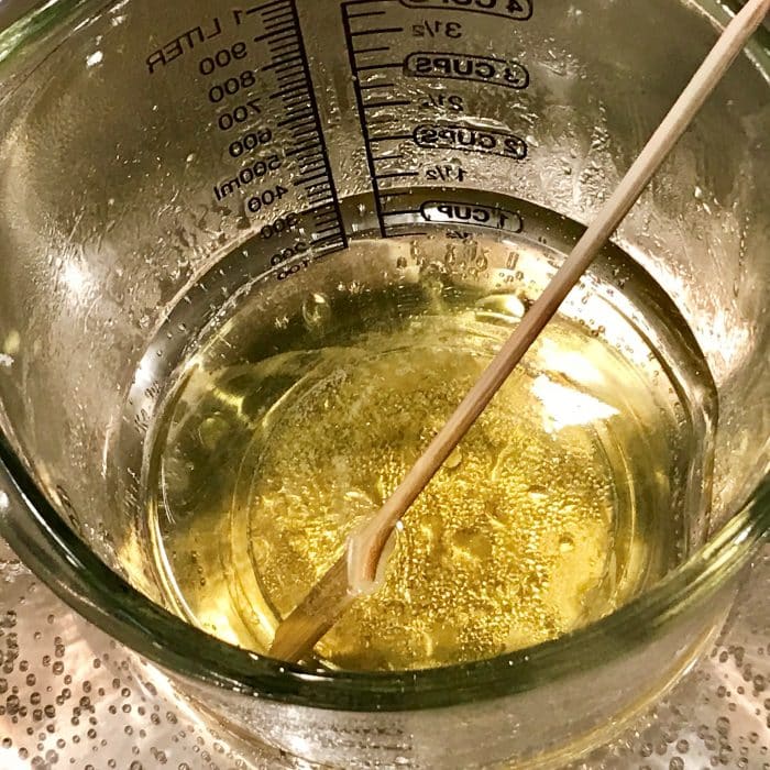 Melted avocado butter and coconut oil in clear heat-safe measuring cup for Copycat Lush Ocean Salt scrub recipe made with essential oils