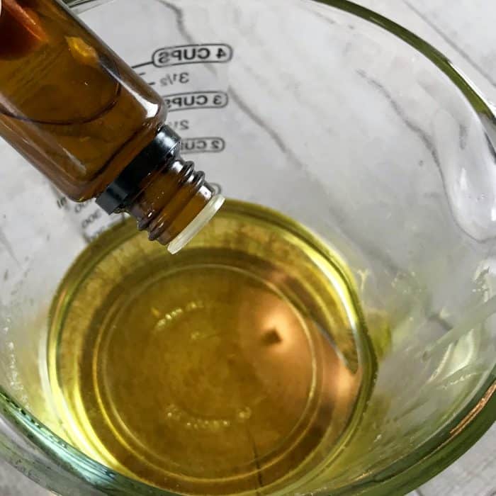adding drops of essential oil to clear heat-safe measuring cup containing melted avocado butter and coconut oil for Copycat Lush Ocean Salt scrub recipe made with essential oils