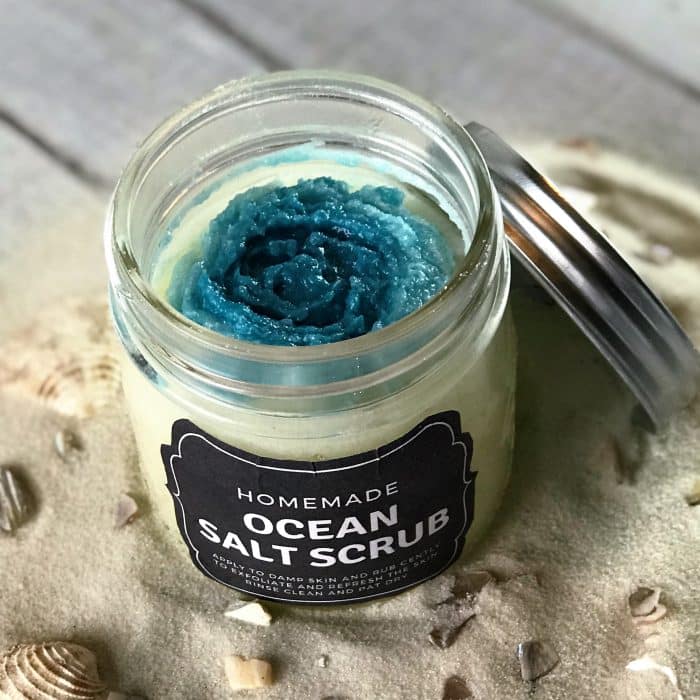 Copycat Lush Ocean Salt scrub recipe made with essential oils on display in clear jar with custom label and ocean blue top layer with sand and seashells