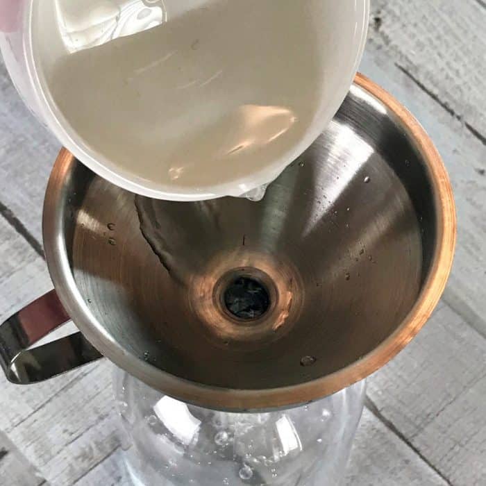 adding hydrogen peroxide through funnel into spray bottle with distilled water for making Homemade Daily Shower Cleaner