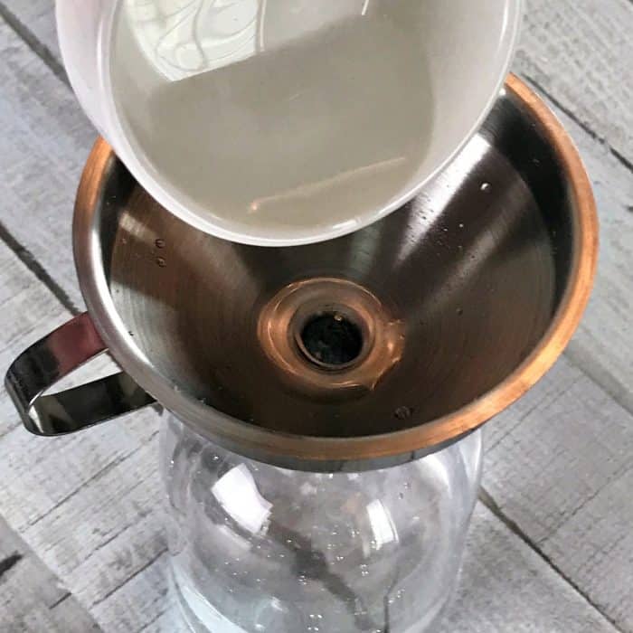 pouring rubbing alcohol through funnel into clear spray bottle, making Homemade Daily Shower Cleaner