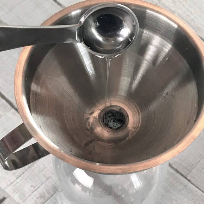 pouring Sal Sads through funnel into clear spray bottle, making Homemade Daily Shower Cleaner