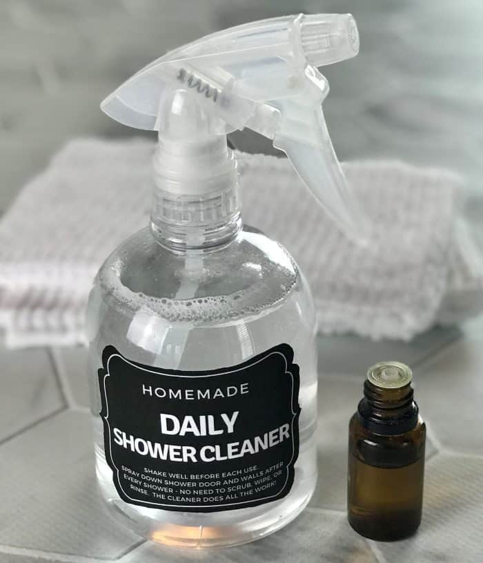 Homemade Daily Shower Cleaner spray bottle with custom label next to essential oil bottle