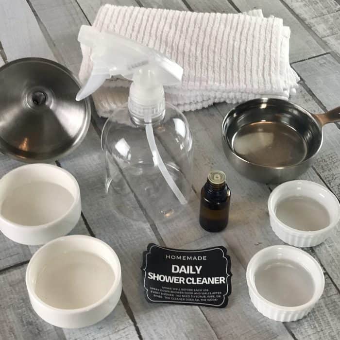 Equipment to make for One Essential Community Daily Shower Cleaner: clear spray bottle, essential oil bottle, measuring cup, funnel, towel, ramekins
