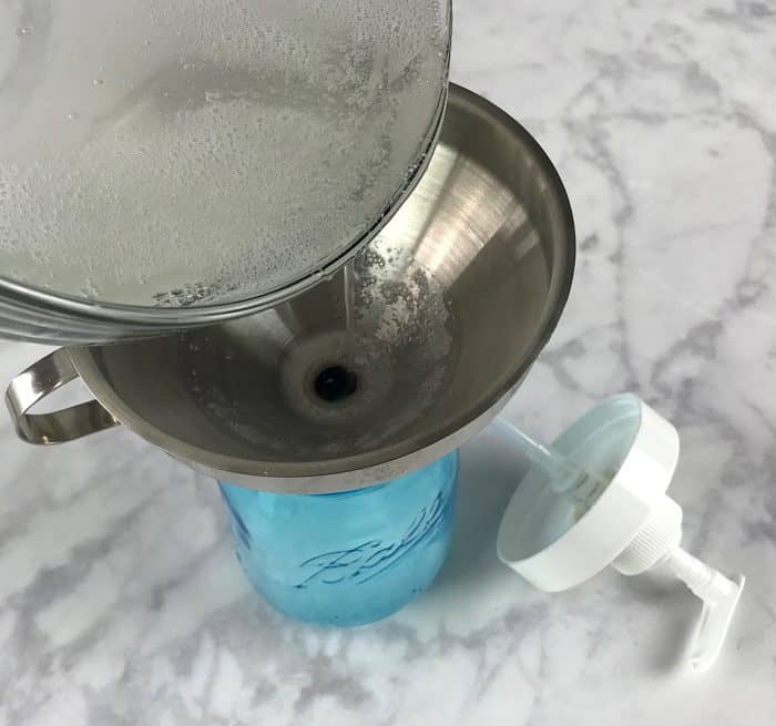 pouring the homemade dish soap through funnel into glass mason jar soap dispenser