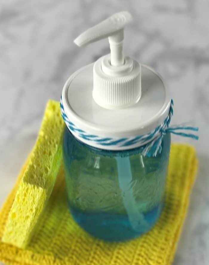 homemade dish soap recipe {made with essential oil} in mason jar soap dispenser on top of yellow dish cloth and next to kitchen sponge