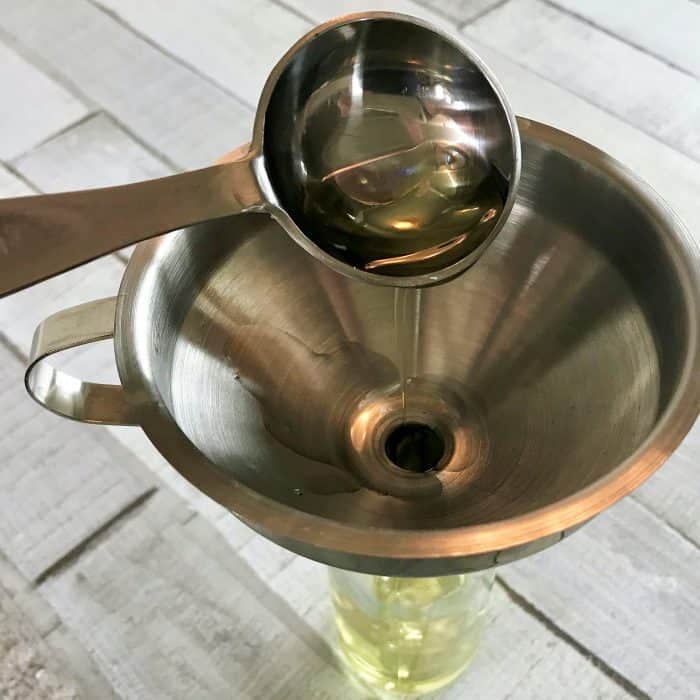 adding avocado oil to funnel and glass spray bottle for homemade hair serum