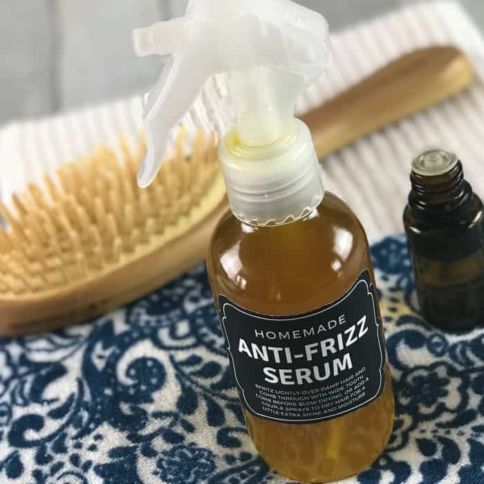 homemade anti-frizz serum in spray bottle with essential oil bottle, detangling hair brush, and a couple towels