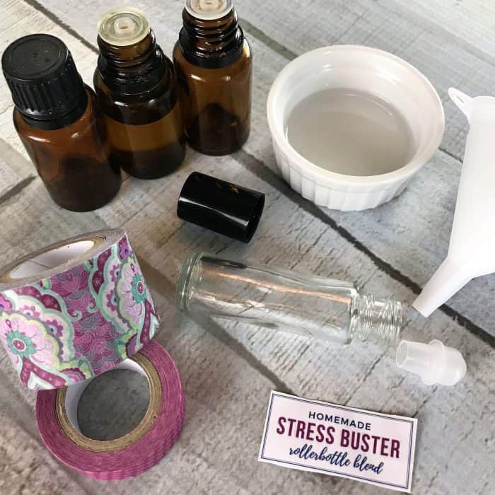 Stress Buster Roller Bottle Blend supplies - 3 essential oil bottles, empty rollerball bottle, free printable label, fractionate coconut oil in small bowl, funnel, washi tape
