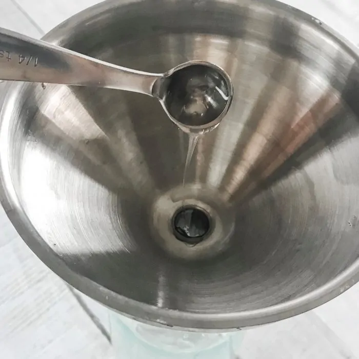 measuring spoon adding Castile soap to funnel