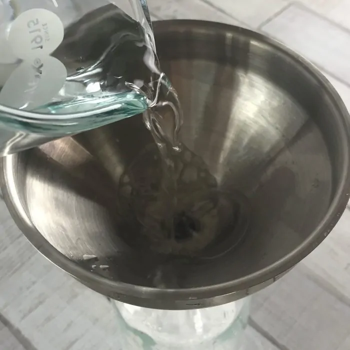 measuring cup adding white vinegar to funnel