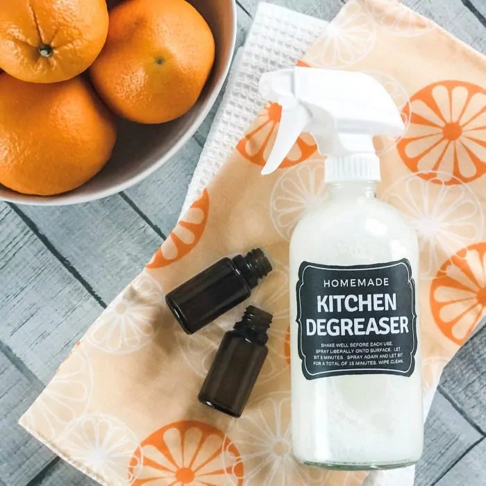 orange and lemon essential oil bottles on orange towel next to homemade kitchen degreaser spray bottle