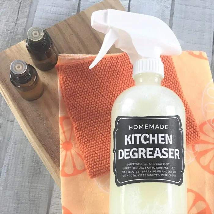 citrus kitchen cleaner on orange towels and wooden board next to essential oil bottles