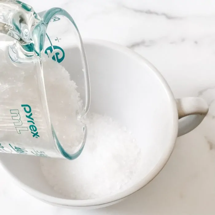 glass measuring cup pouring sea salt into bowl