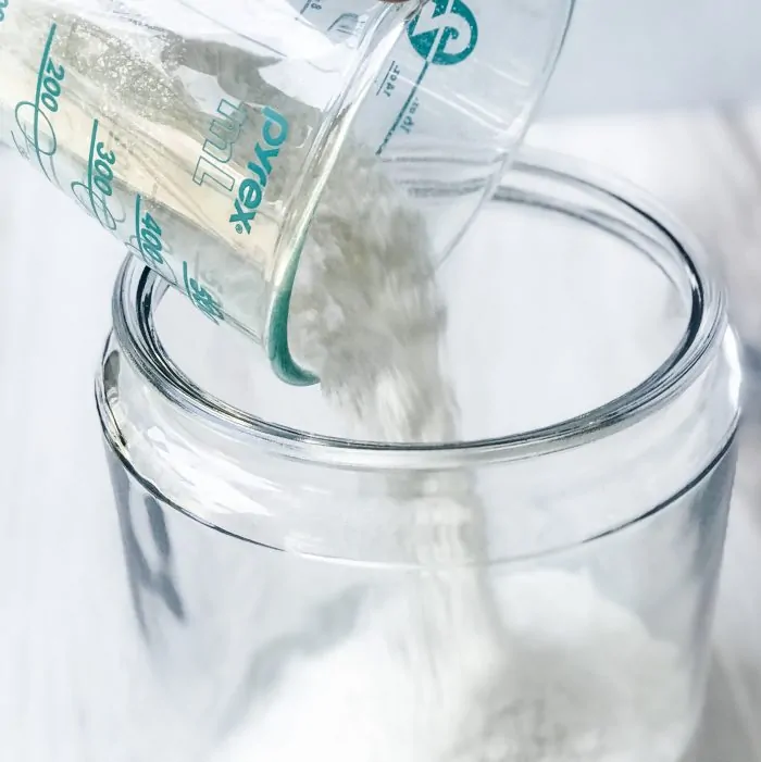 measuring cup pouring soap flakes into canister