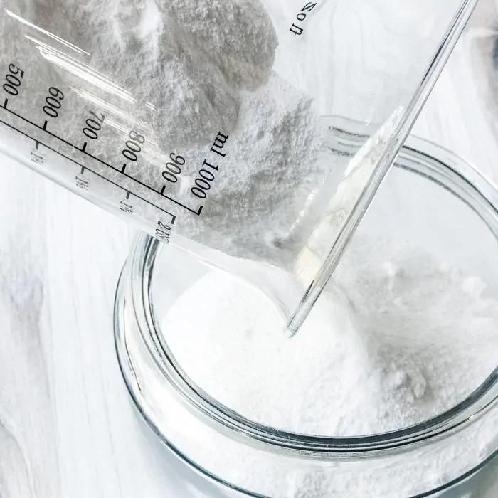 measuring cup pouring borax into canister to make homemade natural laundry detergent