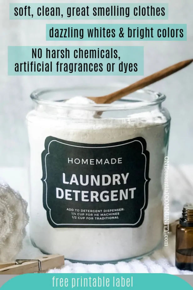 DIY natural laundry soap in large glass canister with free printable label, essential oil bottle, clothes pins, and fluffy white towels surround the canister