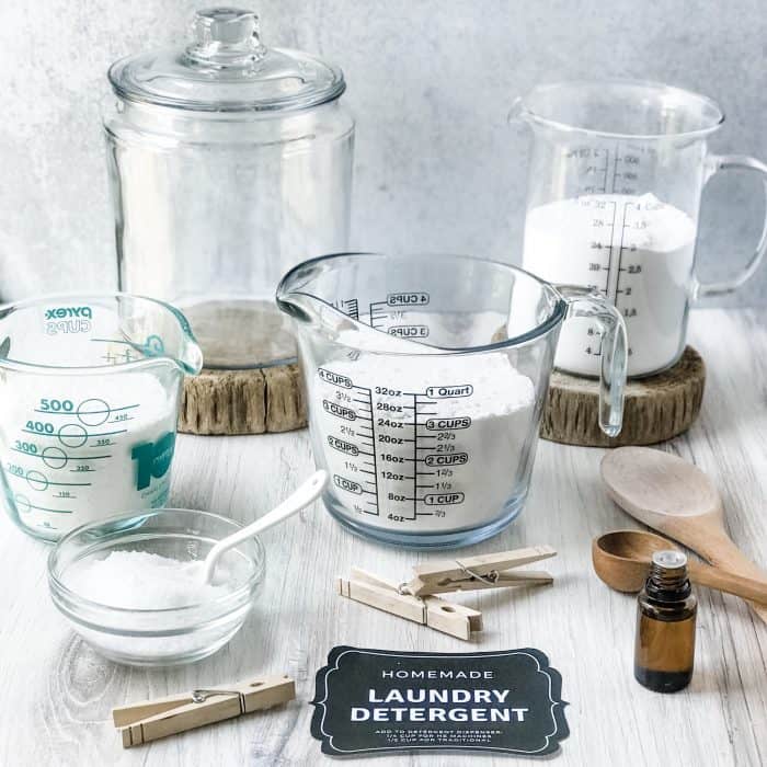 ingredients for making your own natural laundry soap powder - soap flakes, super washing soda, borax, Epsom salt, essential oil, large glass canister, and free printable label