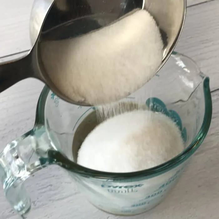 adding non-gmo sugar to vanilla oleoresin and coconut oil in glass measuring cup