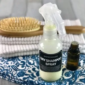 DIY dry shampoo spray next to hair brush and essential oil bottle