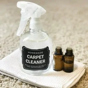 DIY carpet cleaner spray and two essential oil bottles on white cloth and carpet