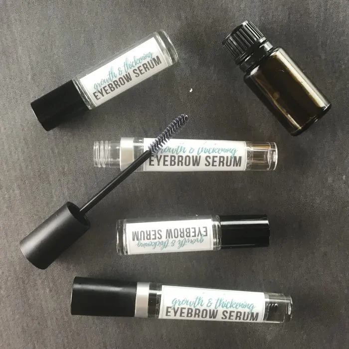 several bottles of homemade eyebrow growth serum, essential oil bottle, and applicator wand