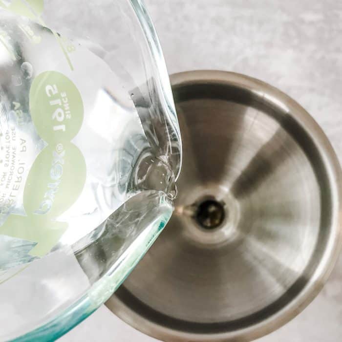 adding white vinegar to homemade furniture polish through a funnel