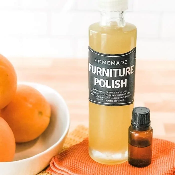 Homemade DIY furniture polish in custom bottle with bottle of sweet orange essential oil and bowl of oranges