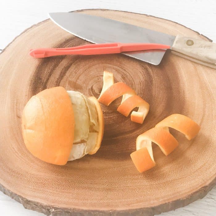 orange with peels, citrus peelers, knife, on cutting board