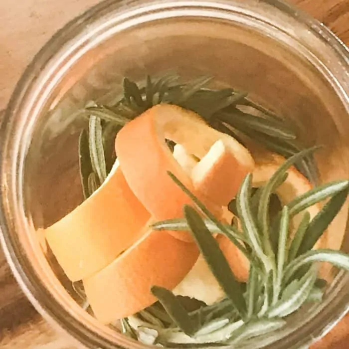 overhead shot of orange peels and rosemary sprigs in clear glass jar, ingredient for floating scented candles with essential oils