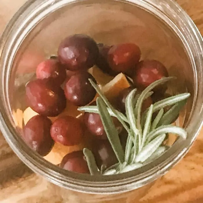 overhead photo of cranberries, orange peels, rosemary sprigs in jar, ingredient for floating scented candles with essential oils