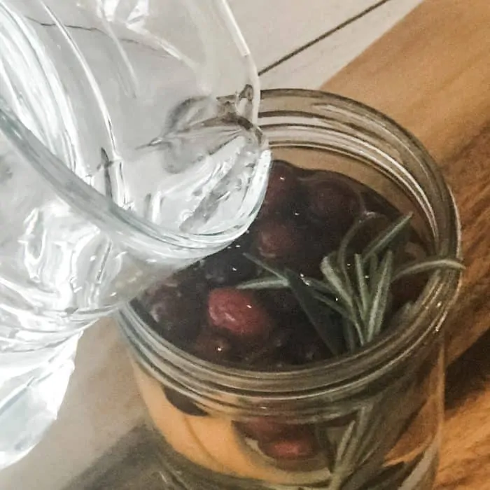adding water to mason jar with cranberries, orange peels, and rosemary sprigs, making floating scented candles with essential oils