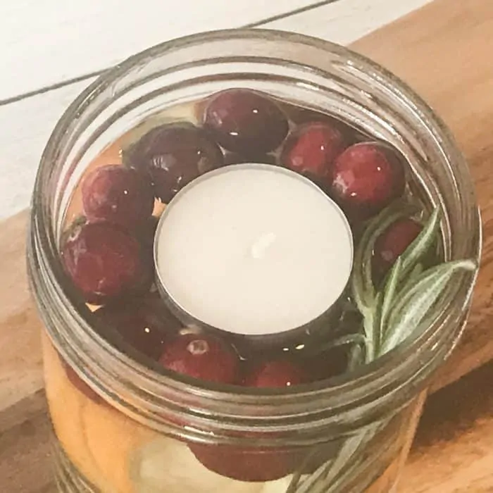 placing floating candle on top of water-filled mason jar with cranberries, orange peels, rosemary, floating scented candle with essential oils christmas candle