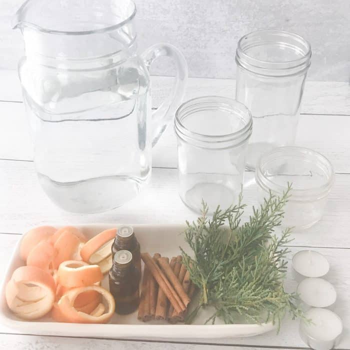 orange peels, rosemary sprigs, cranberries, essential oil bottles, pitcher of water, clear glass jars, essential oil bottles, ingredients for scented floated candles with essential oils