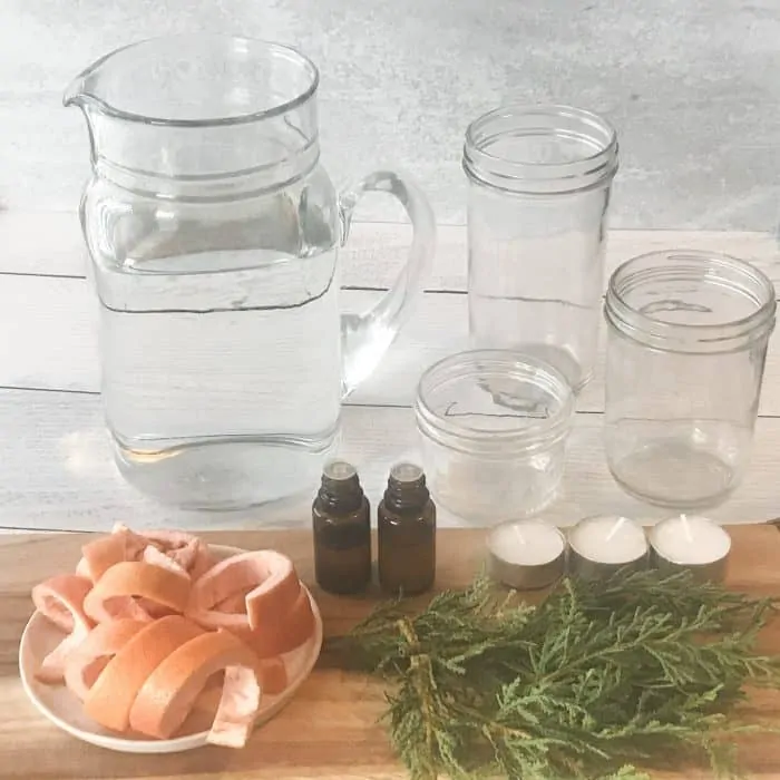orange peels, rosemary sprigs, essential oil bottles, pitcher of water, clear glass jars, essential oil bottles, ingredients for scented floated candles with essential oils
