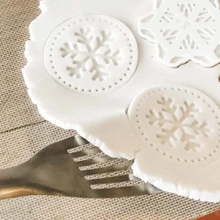 Lifting salt dough with spatula with snowflake cookie cutter and cookie stamp shapes cut out