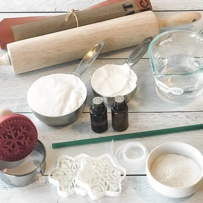 Layout of salt dough ingredients and tools, baking soda, cornstarch, essential oils, silpat, rolling pin, measuring cup and spoons, snowflake cookie cutters