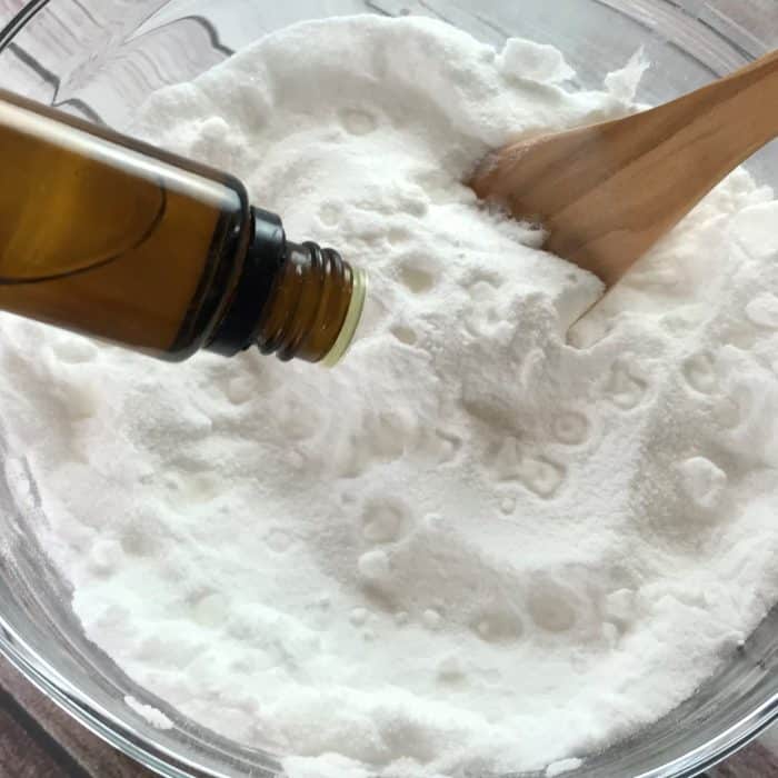 adding drops tea tree essential oil from essential oil bottle to baking soda and citric acid in glass bowl for making essential oil facial steamer tabs