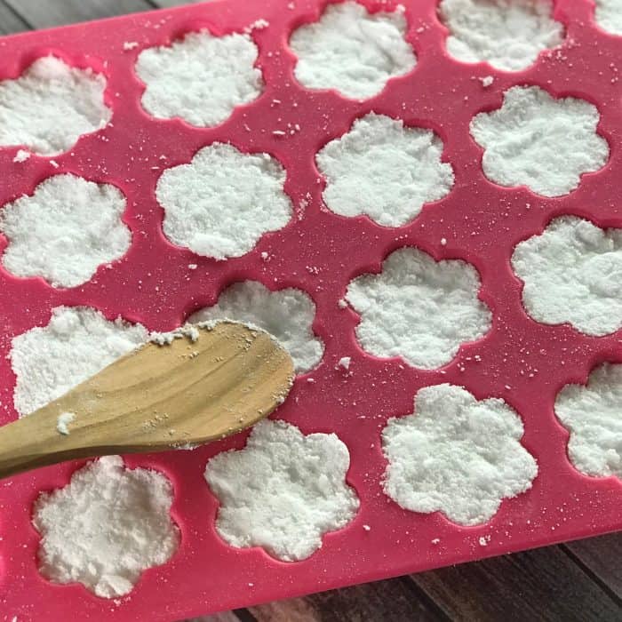 pressing mixture for tea tree essential oil facial steamer tabs into flower shaped silicone molds with wooden spoon