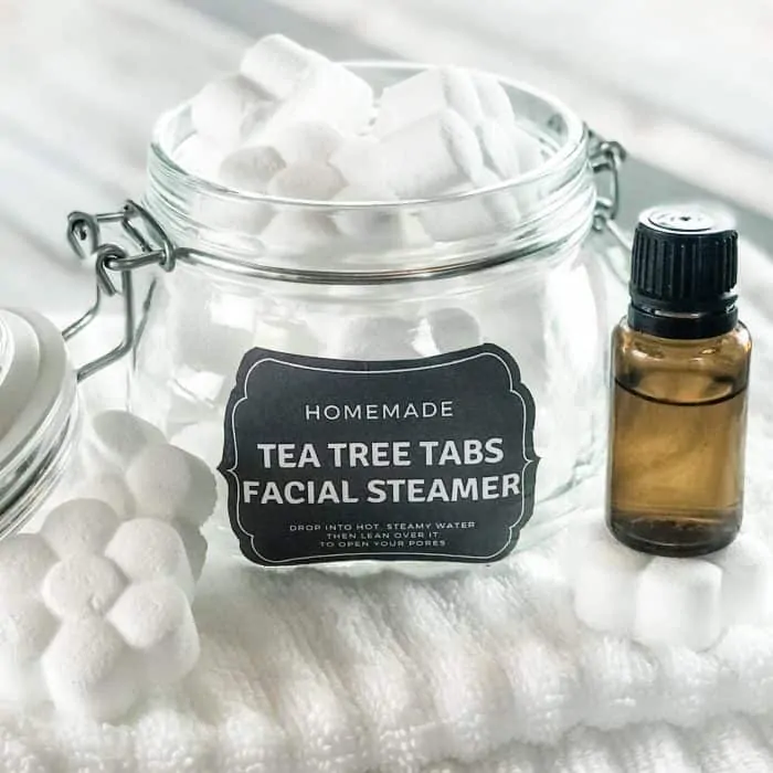 homemade tea tree tabs facial steamer with essential oil in open glass jar with custom label next to essential oil bottle