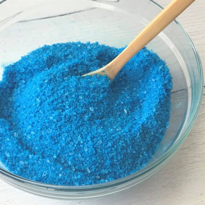 stirring together apricot kernel oil, orange essential oil, frankincense essential oil, myrrh essential oil to Epsom salt, sea salt, baking soda, blue lake coloring, silver mica in glass bowl