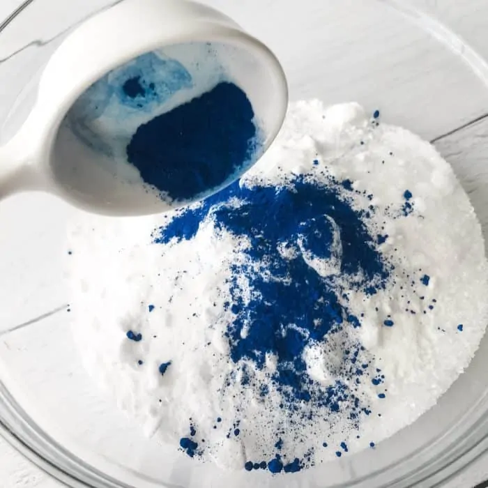 adding blue lake coloring to Epsom salt, sea salt, baking soda in glass bowl