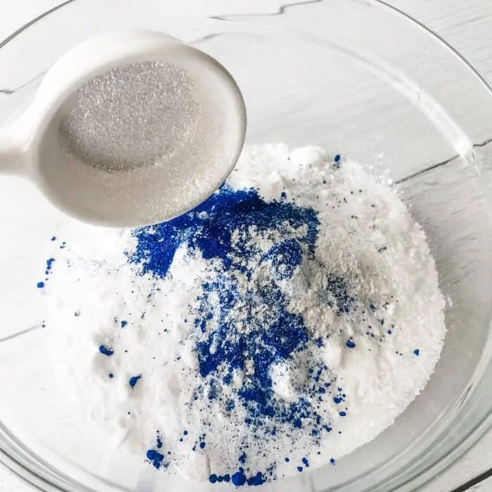 adding silver mica to Epsom salt, sea salt, baking soda, blue lake coloring in glass bowl