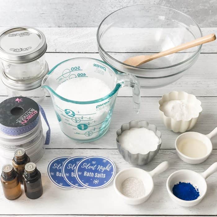 Silent Night Bath Salts ingredients display of Epsom salt, sea salt, blue coloring, mica, essential oil bottles, measuring cups and spoons, jars and labels